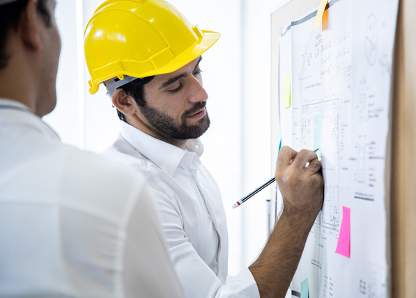 Joven ingeniero con casco dibujando sobre un plano